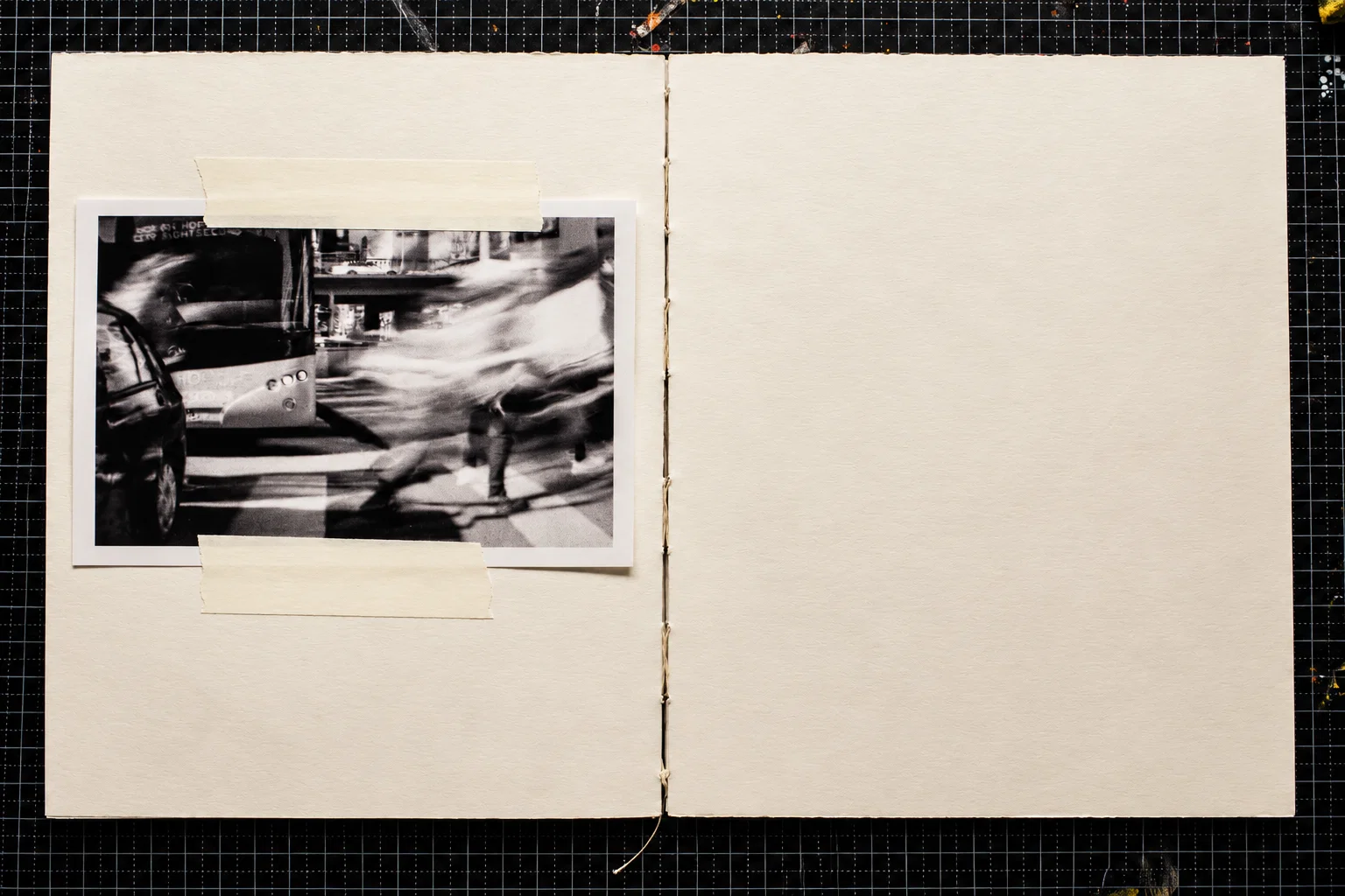 A single black-and-white photograph on the left-hand page shows a bus and a car on a city street, with a pedestrian crossing in front of them. Motion blur stretches the moving figures across the image. The right page is blank.