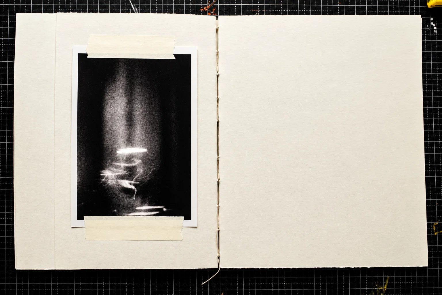A single black-and-white photograph on the left-hand page. Against a nearly black background, thin, irregular trails of white light gather beneath a soft vertical glow. The right page is blank.